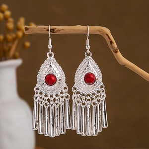 Ethnic peacock earrings with silver tassels and red beads hanging on a wooden branch