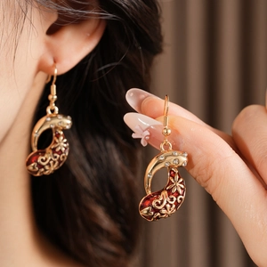 Close-up of vintage gold earrings with red enamel and zircon crystals on a model