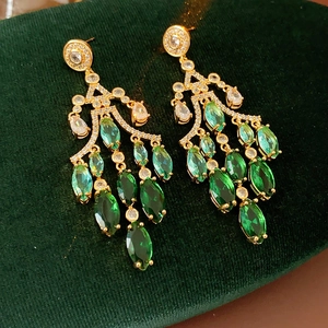 Detail of gold drop earrings with green marquise stones and tassels on green velvet