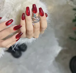 Detail of deep red cat eye press-on nails with a silver snake ring on white fur