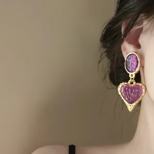 Close-up of vintage heart drop earrings featuring dark red resin on a female model