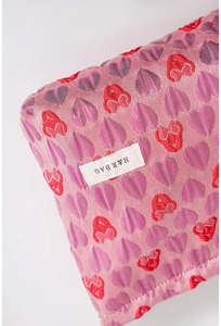 Detailed macro view of pink heart-patterned jacquard fabric with brand label on makeup bag