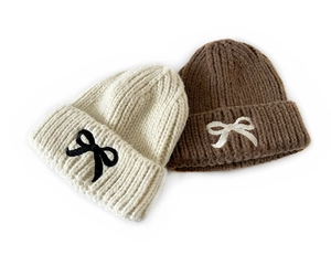 Close-up of winter knit hats with cute bow embroidery in beige and brown colors