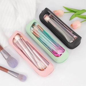 Three travel makeup brush pouches in pink, green, and black with clear windows and brushes