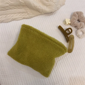 Detail of soft green faux fur pouch on white grid bedding with knitting accessories