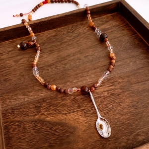 Détail du collier de perles en bois avec un pendentif cuillère argenté dans un plateau