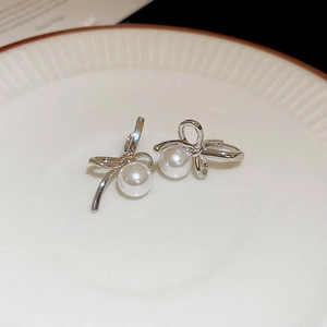 Macro shot of silver bow knot earrings with white pearls on a white ceramic tray