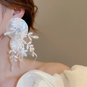 Vue détaillée de longues boucles d'oreilles en dentelle blanche avec broderie de feuilles