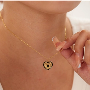 Detail of 18K gold heart necklace with evil eye pendant worn by a model
