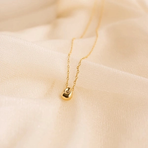 Close-up of golden teardrop necklace with a single zircon pendant on soft beige fabric
