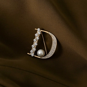 Elegante goldene D-Buchstaben-Brosche mit Kristallen und weißer Perle auf braunem Stoff