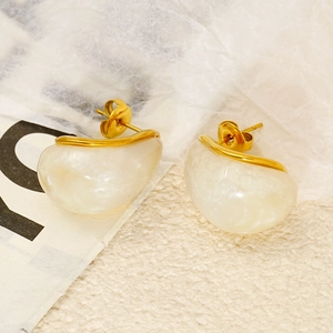 Close-up of golden irregular arc earrings with white resin inlay on textured surface
