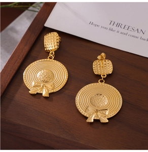 Detail view of gold straw hat earrings with bow design on a wooden tray and card