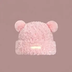 Detail einer rosa Plüschstrickmütze mit Bärenohren und dekorativem Aufnäher