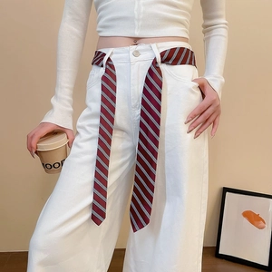 Detail of a dark red striped silk ribbon belt styled with denim jeans for a chic look