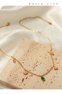 Detail of gold titanium necklace with emerald-cut green stone and sun pendants