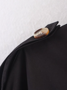 Detailed macro shot of black trench coat shoulder strap with amber button finish