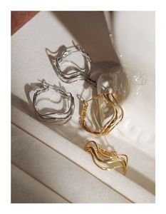Detailed view of silver and gold wavy hoop earrings on soft beige fabric background