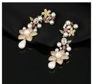 Detail of flower earrings with colorful zircons and drop pearl on black surface
