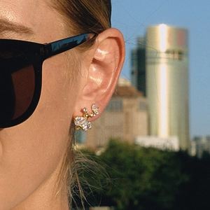Close-up of gold insect stud earrings with white zircons worn on ear in city sunlight