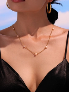 Close-up of golden O-chain necklace with pink freshwater pearls on a model wearing black