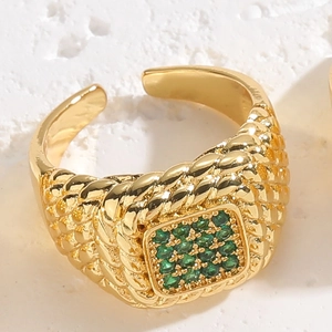 Macro detail of gold braided band ring with square green zircon setting on stone base