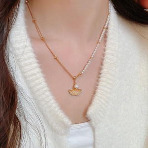 Close-up of gold ginkgo leaf necklace with a white pearl and asymmetrical chain detail