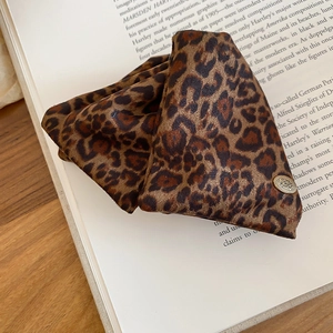 Detail of leopard print fabric hair claw clip with vintage gold button on a book