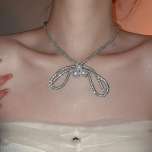Close-up of elegant rhinestone bow necklace featuring three large white pearls on a model