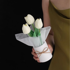 Detailed view of hand-held artificial white tulips in a rustic paper wrap with bow