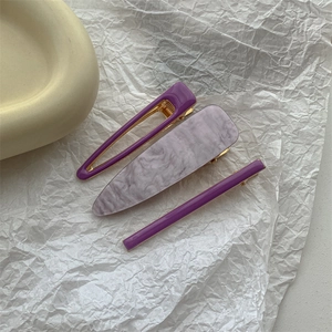 Detail view of purple geometric and marble hair clips with golden metal base on white paper