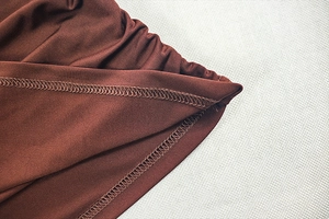 Detailed close-up of brown knit fabric with overlock stitching and ruched texture details