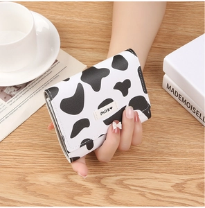 Close-up of mini cow print tri-fold wallet held in hand with Milk tag detail