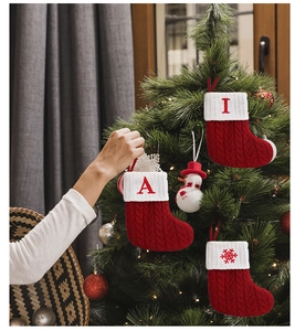 Detail of hand hanging a red knitted Christmas stocking with white embroidered letters