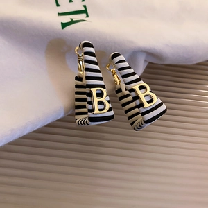 Detail of earring with black white stripes and golden letter B on beige stand