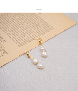 Close-up of vintage knotted gold earrings with stacked freshwater pearls on book pages