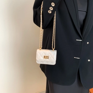 Chic white mini quilted chain bag with gold twist lock on a black suit blazer background