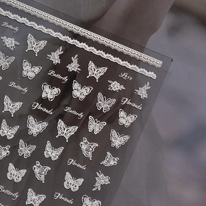 Detailed view of white lace butterfly and floral nail stickers with elegant lettering