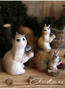 Three plush Christmas squirrel ornaments with pine cones and red berries on wood surface