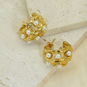 Detailed macro view of gold-plated scalloped earrings with pearls on a textured stone