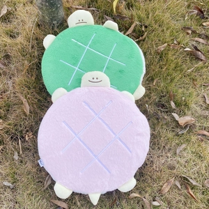Outdoor view of turtle-shaped plush cushions in green and pink with soft grid texture