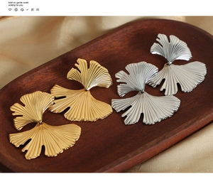 Detailed close-up of ginkgo leaf earrings in gold and silver finish on silk fabric