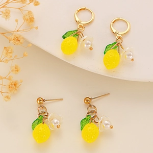 Detailed macro view of yellow lemon earrings with green leaves and small white pearl flowers