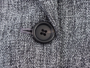 Macro shot of herringbone tweed fabric detail and black resin button on grey blazer