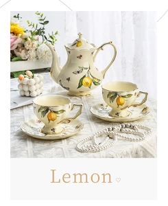 Close-up of lemon pattern ceramic teapot and cups with gold rims on lace tablecloth
