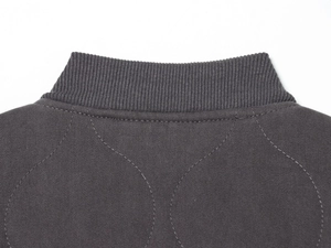 Close-up of dark grey bomber jacket featuring ribbed collar and quilted twill fabric texture