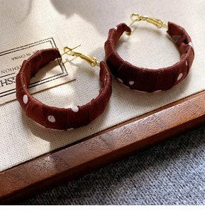 Close-up of retro brown polka dot fabric wrapped hoop earrings on beige textured fabric