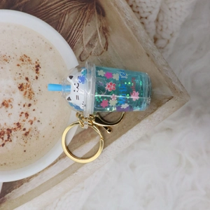 Detail of creative cat milk tea cup keychain with blue liquid glitter and cat doll