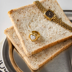 Detail shot of vintage gold heart pearl ring and square watch on minimalist bread display