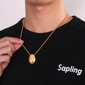 Close-up of a polished gold oval pendant on a woven chain worn on a black shirt